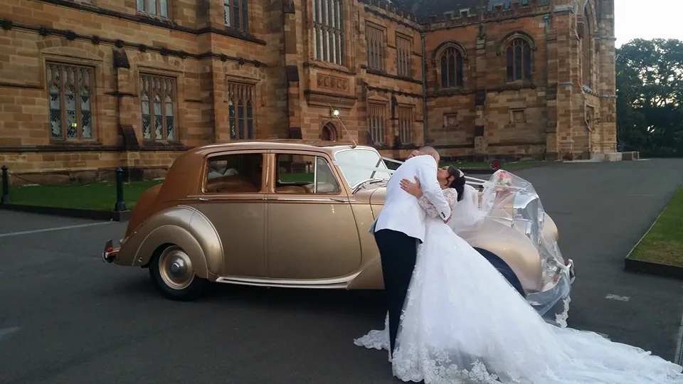 Couple kissing beside gold wedding car